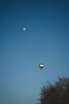 A serene hot air balloon floats beneath a clear sky with a visible moon in Columbia, Missouri.