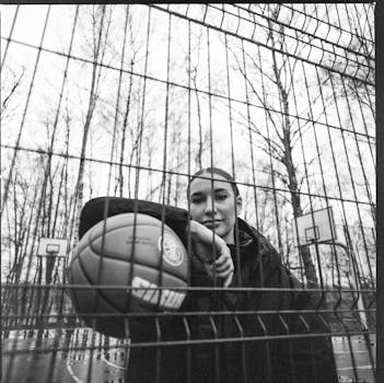 A black and white portrait of a person holding a basketball on an outdoor court.