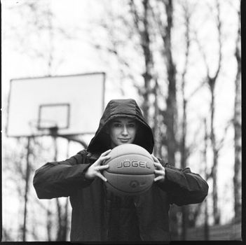 Black and white image of person holding basketball outdoors in winter.