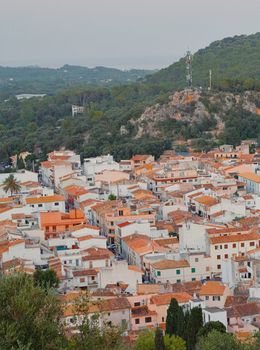 Charming aerial view of a Spanish village with distinctive red rooftops near wooded hills.
