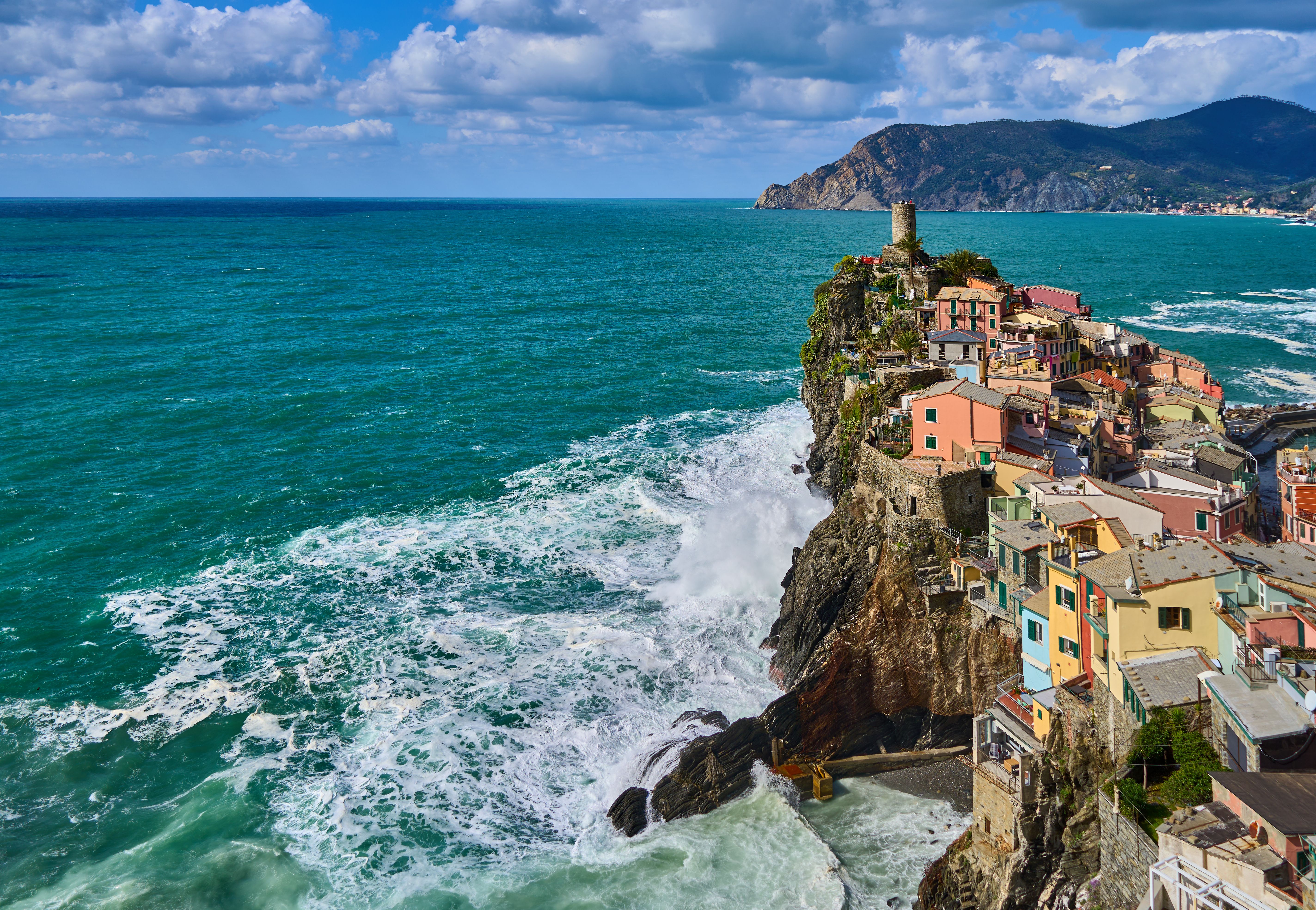 A scenic view of Vernazza, a coastal village in Cinque Terre, Italy, with waves crashing against the cliffs.