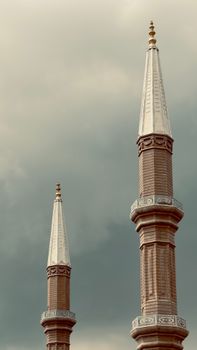 Vertical shot of two intricate minarets with a dramatic cloudy background.
