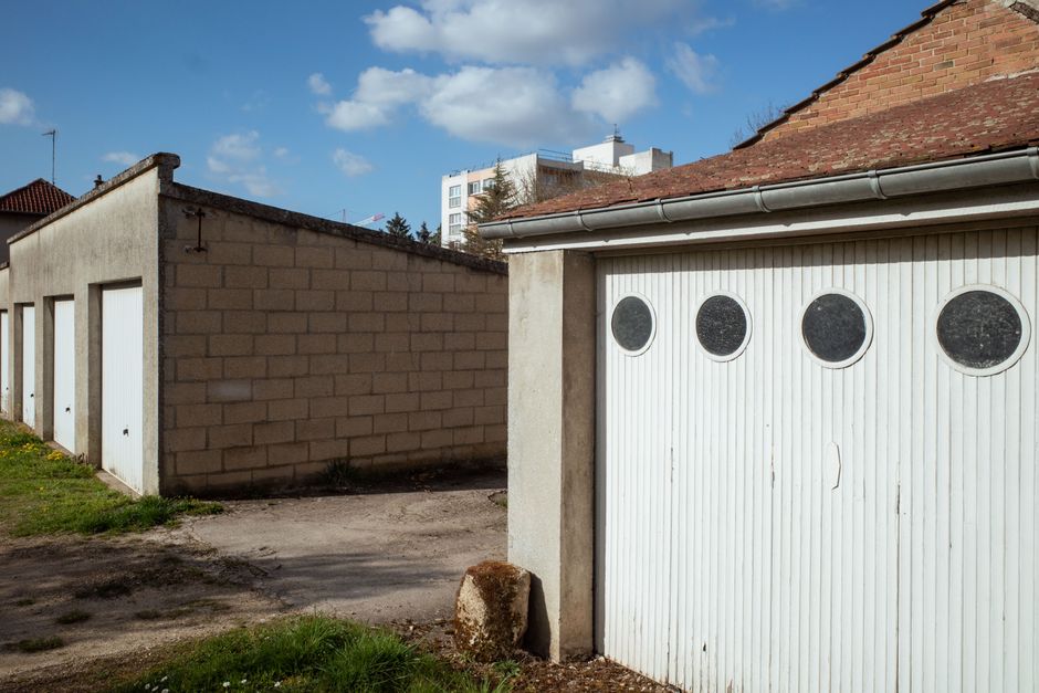 Series of garages with distinctive round windows under a clear blue sky in Compiègne, France.