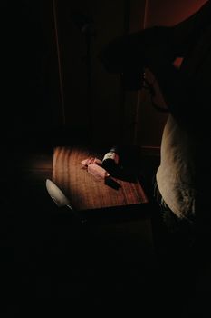 Moody kitchen scene with wine bottle and slicing knife on wooden table.