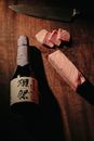 A bottle of premium sake and slices of wagyu steak on a rustic wooden board with a knife.
