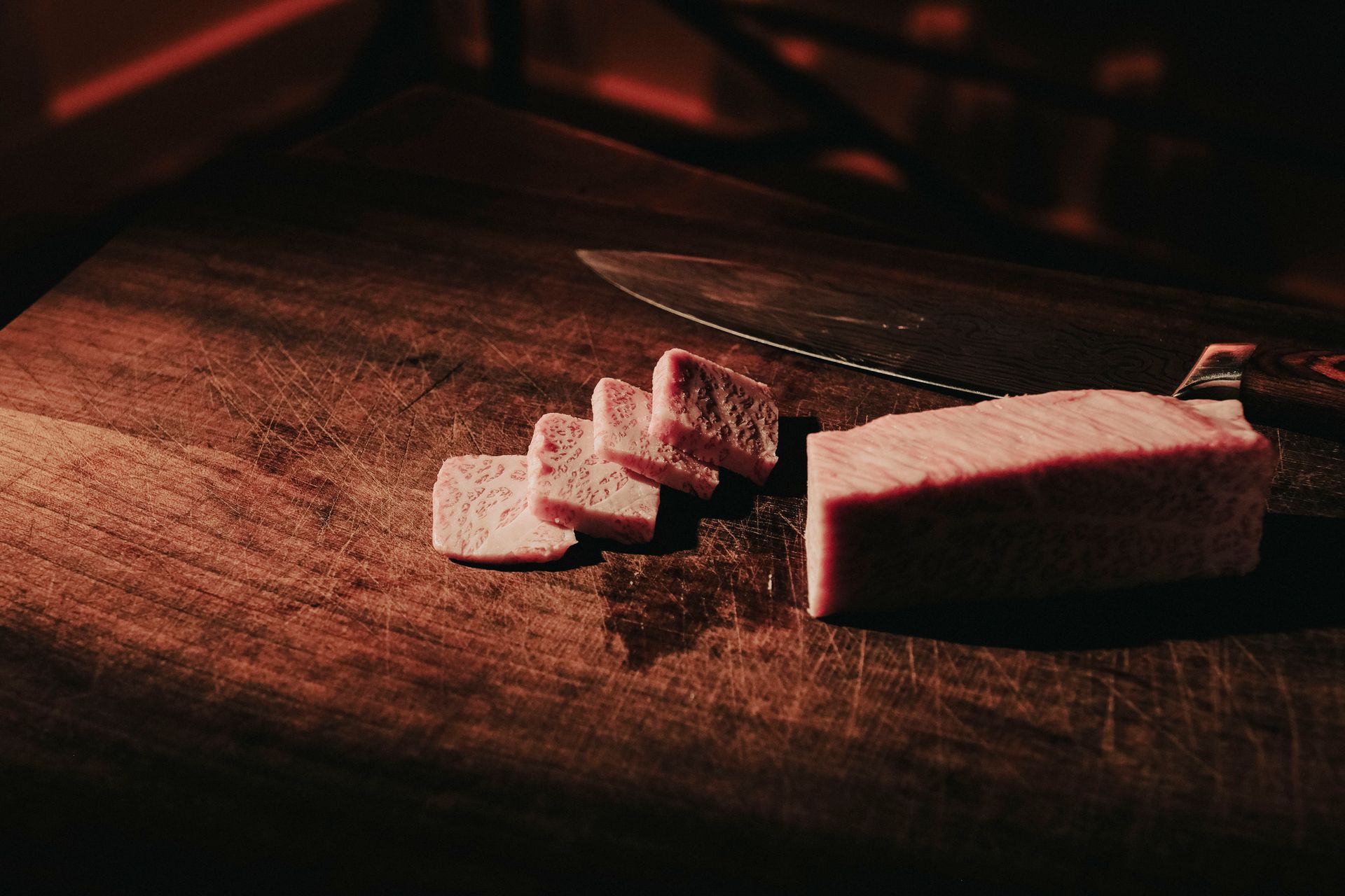 Close-up of sliced taro with knife on a dark wooden board. Moody lighting.