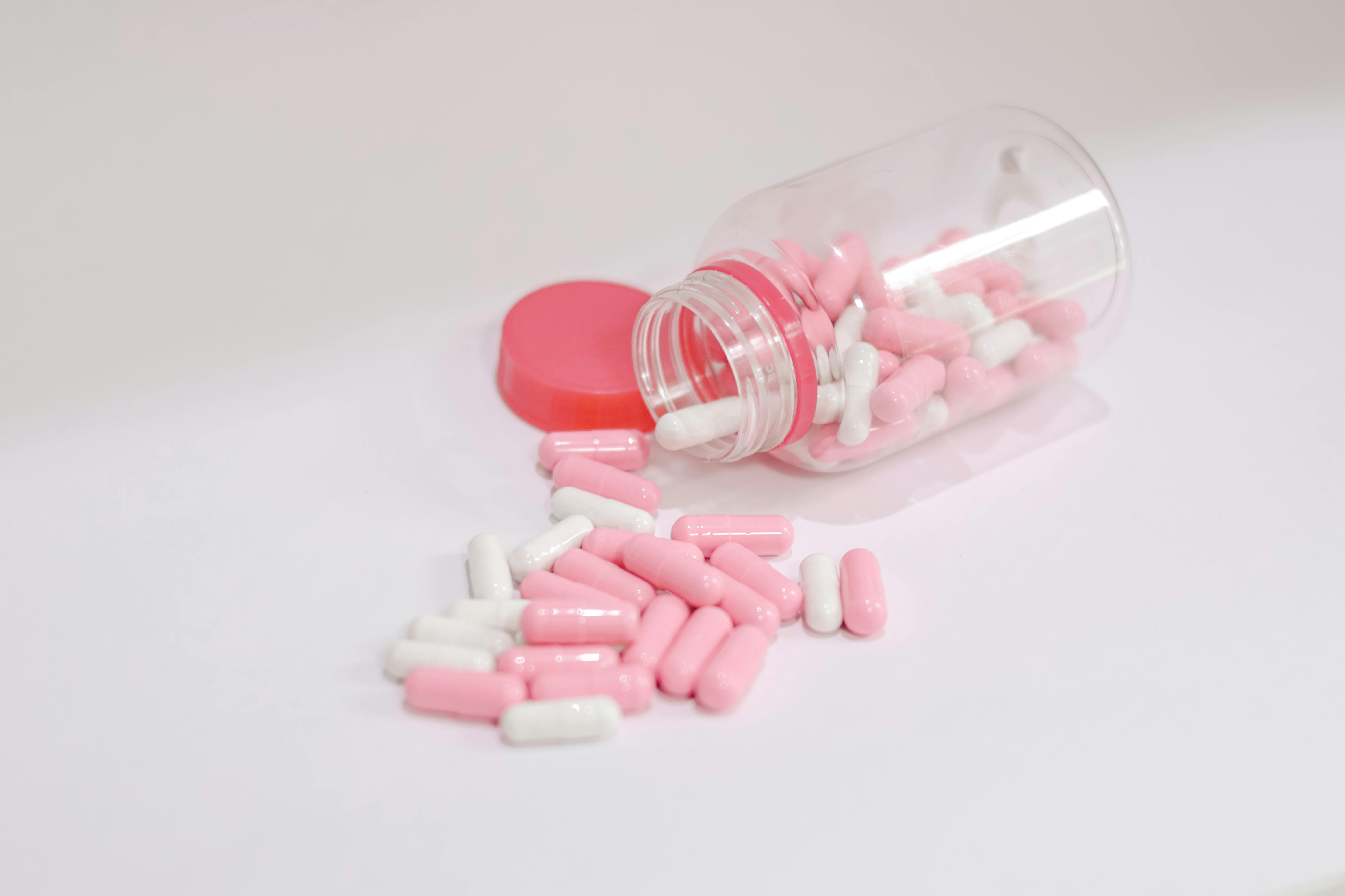 medicare supplement plans Florida reviews - Pink and white capsules scattered from a tipped-over bottle on a white surface, symbolizing health care.