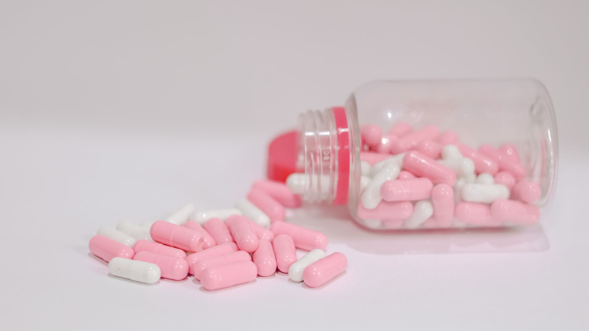 Hypersomnia Treatment Medication: Comprehensive Guide Close-up of pink and white capsules spilled from a plastic bottle on a white background — hypersomnia treatment medication