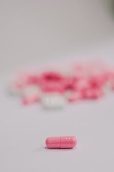 A vivid pink capsule in sharp focus with a soft, blurred background of more pills.