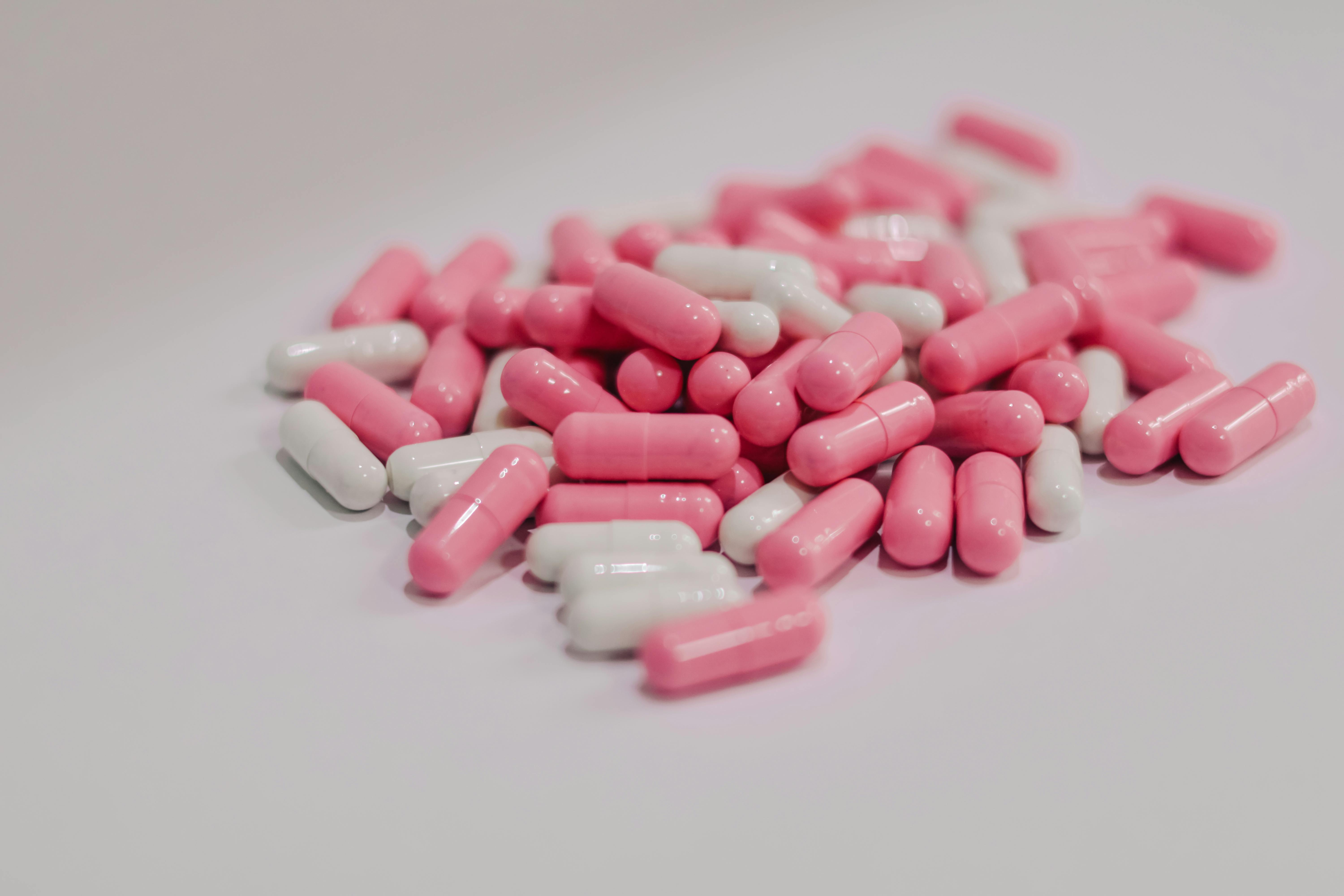 Close-up of pink and white pharmaceutical capsules scattered on a white surface.