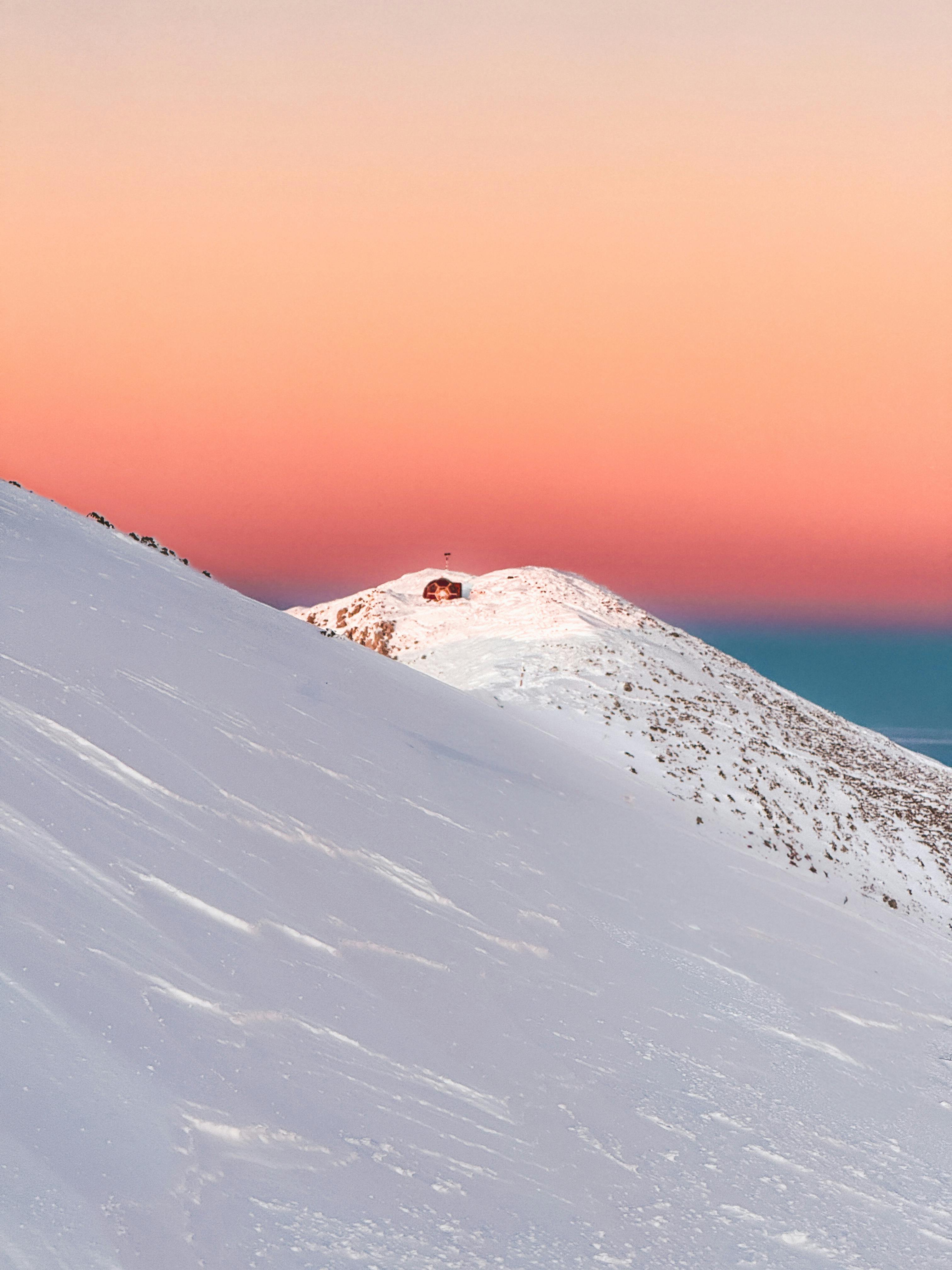 A peaceful winter sunrise over a snowy mountain ridge with a remote cabin.