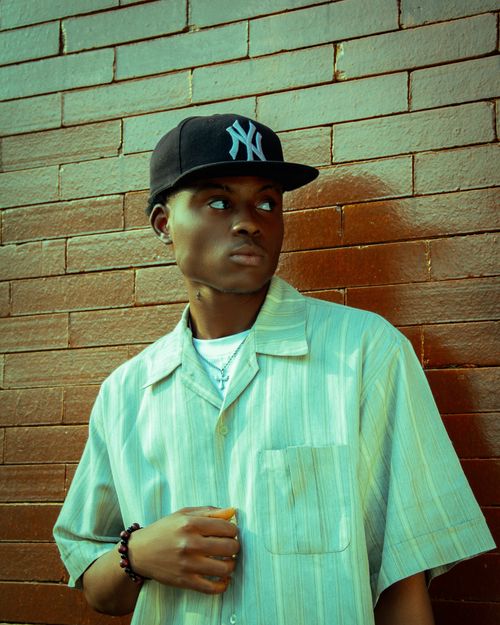 Free Young male wearing cap and shirt, standing by a brick wall with a thoughtful expression. Stock Photo