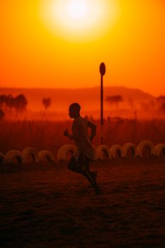 Silhouette of a person running against a vivid orange sunset with a dramatic sky and warm landscape.