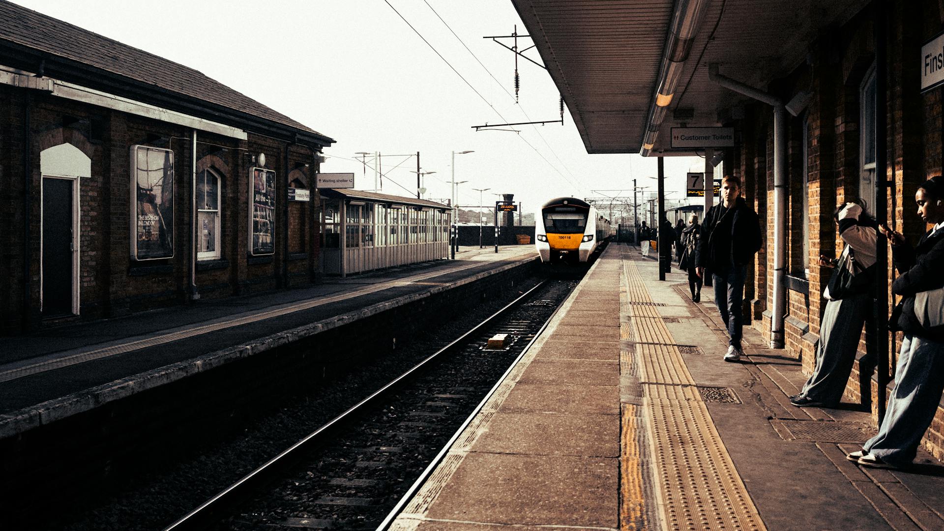 Commuters wait on a platform as a train approaches at a London railway station.