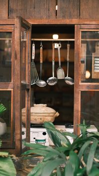 Cozy rustic kitchen view through window featuring hanging utensils and green plants.