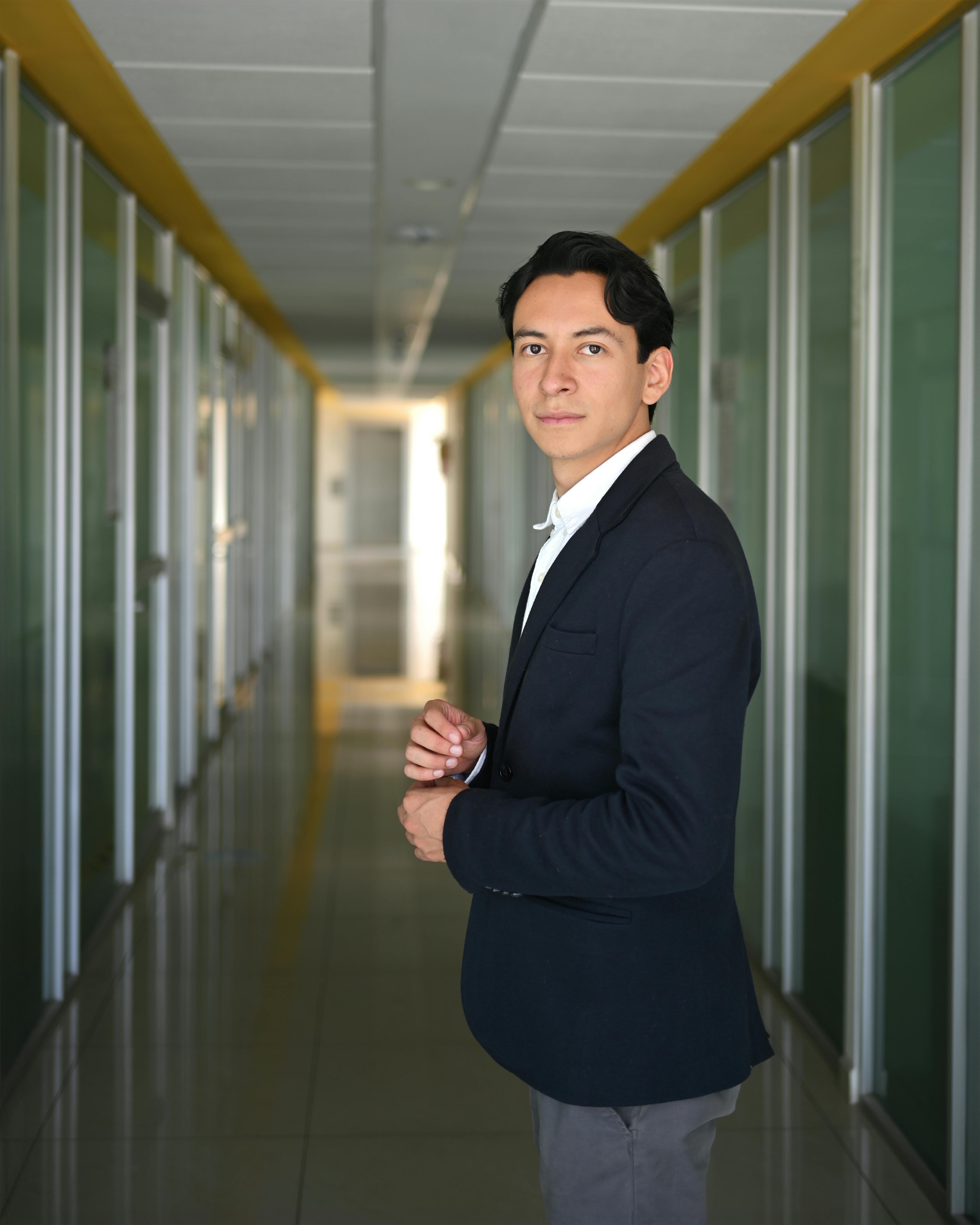 Young man in a suit standing in a modern office corridor.