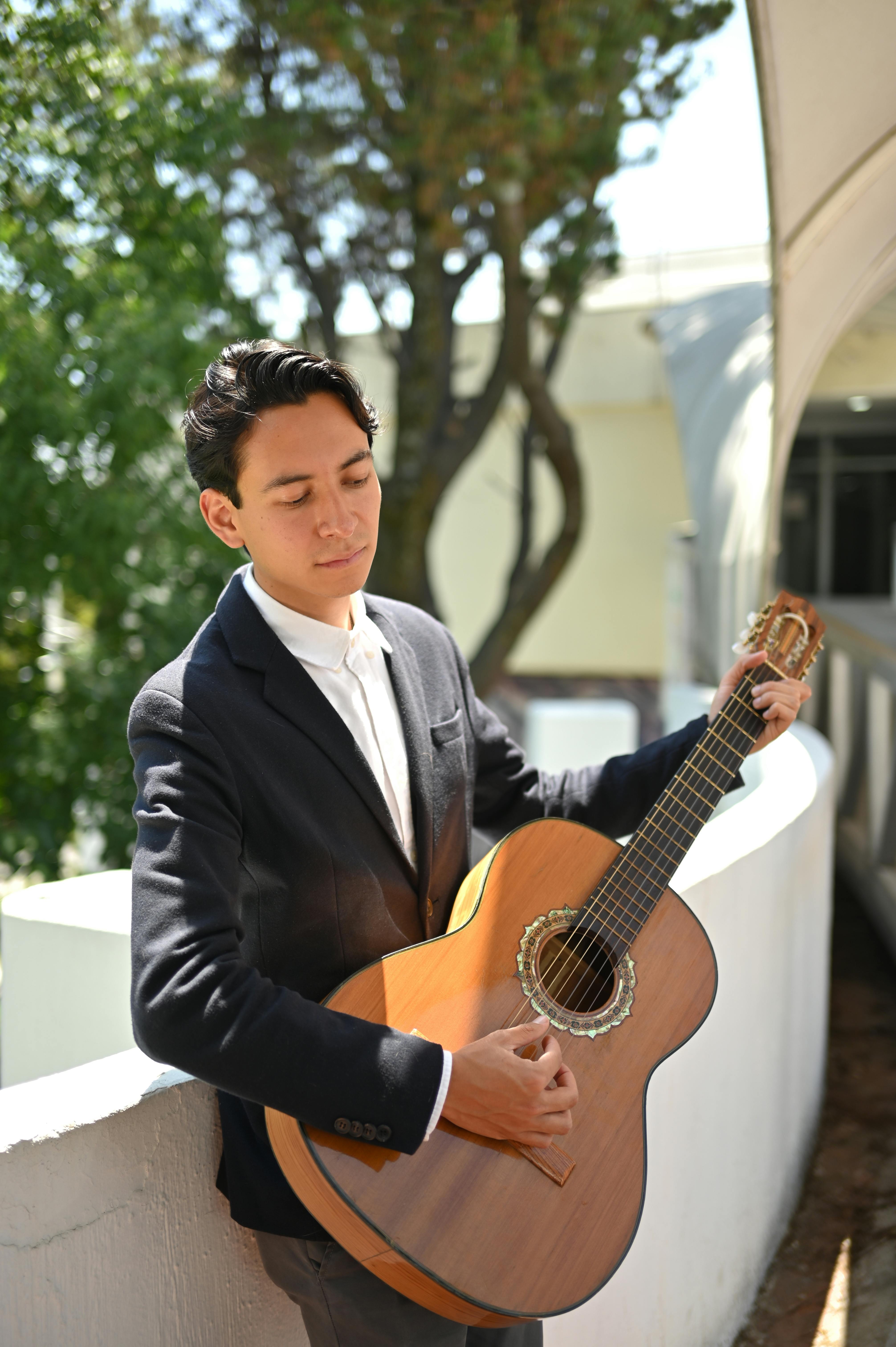 Young man in formal attire playing guitar on balcony, enjoying music.