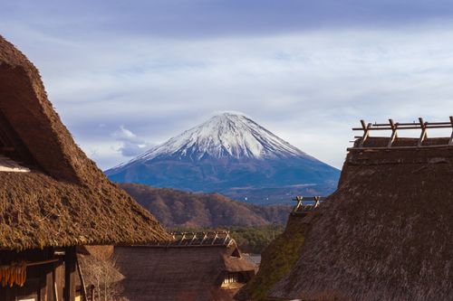 Free Traditional thatched roofs with the iconic Mount Fuji in the background, capturing the serene Japanese landscape. Stock Photo