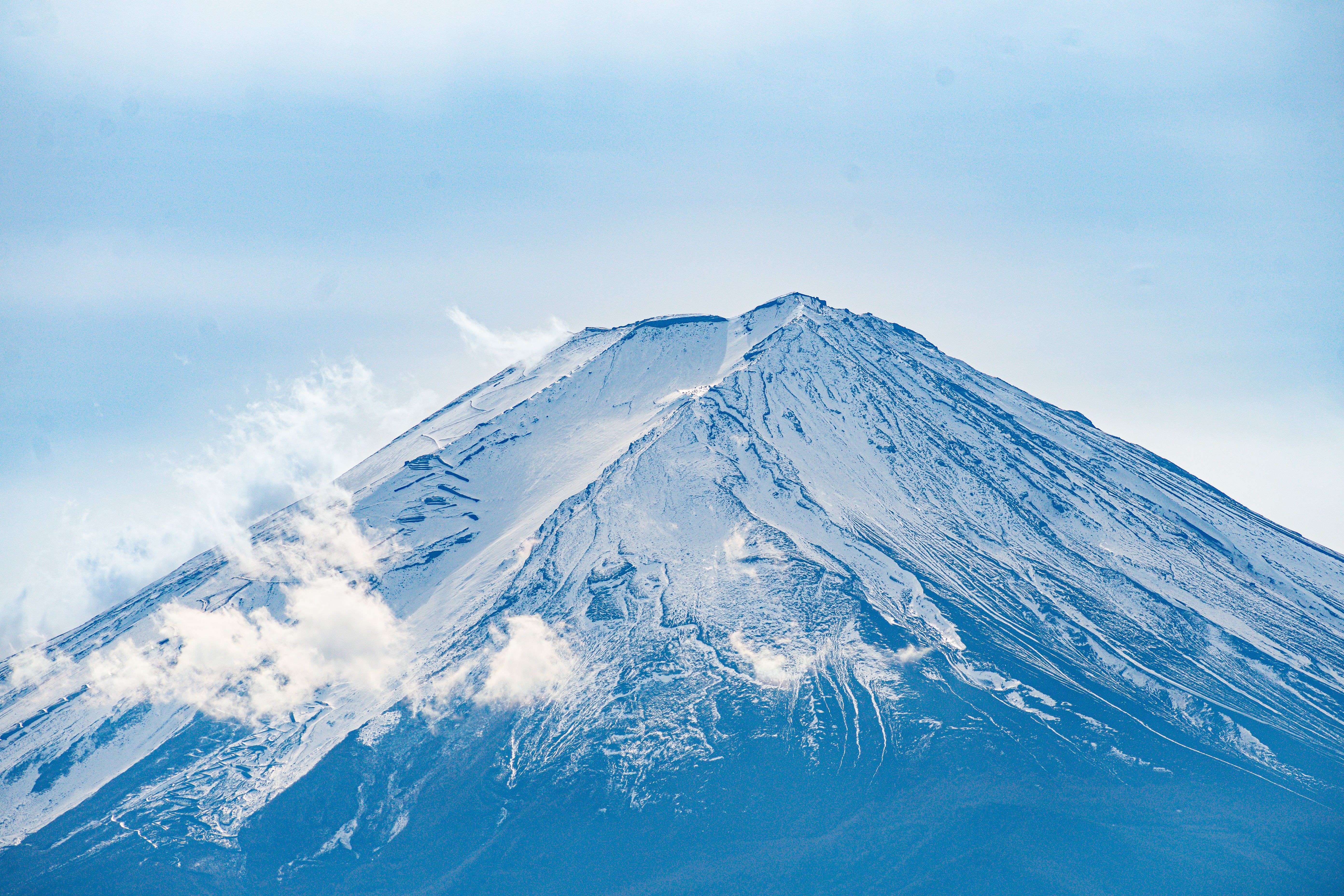 A breathtaking view of Mount Fuji with snow-capped peaks and clouds against a blue sky.