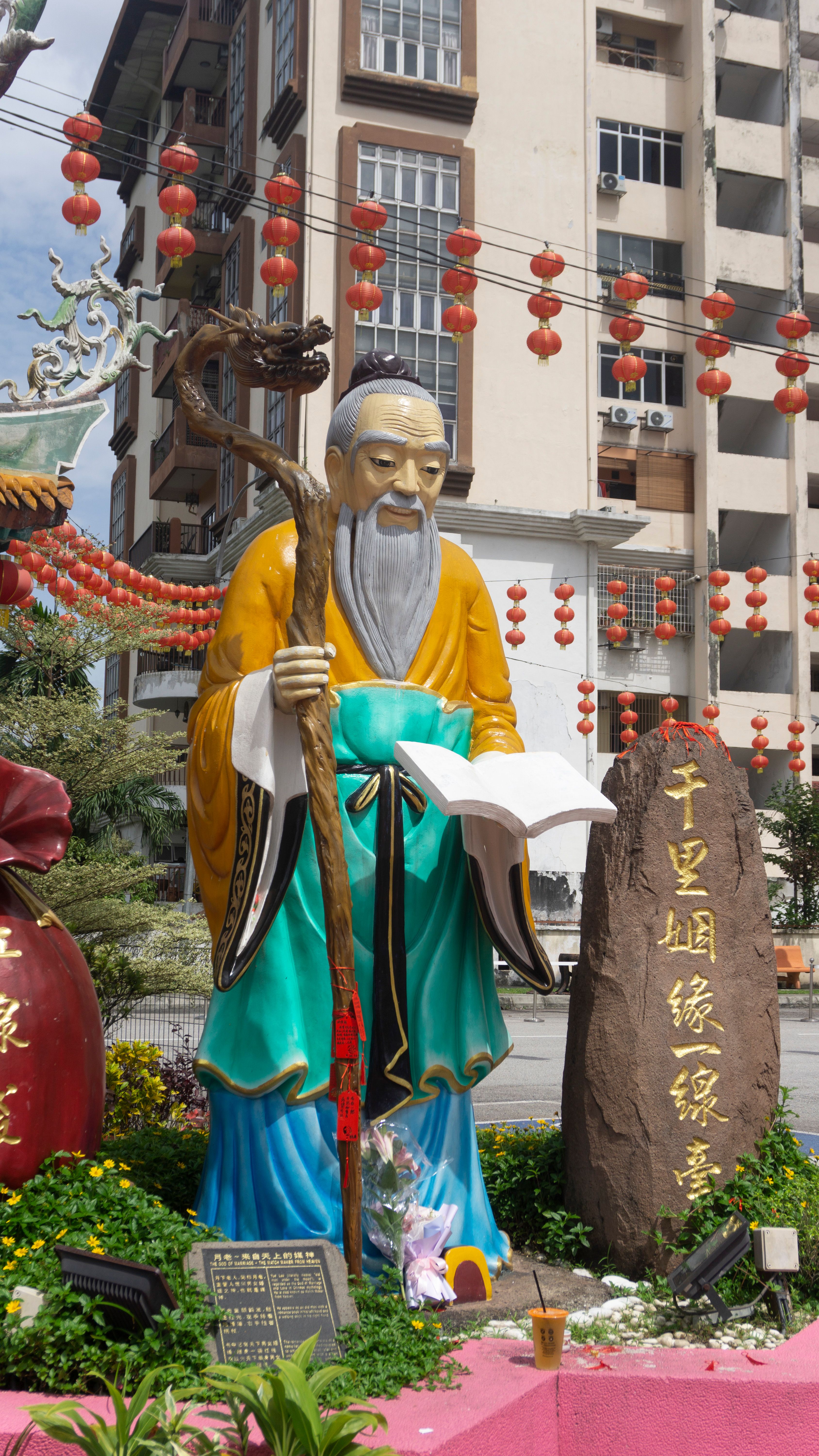 Vibrant Buddhist statue with lanterns in a cityscape background.