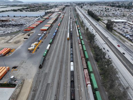Aerial perspective of a busy train yard with freight trains and cargo containers in California.