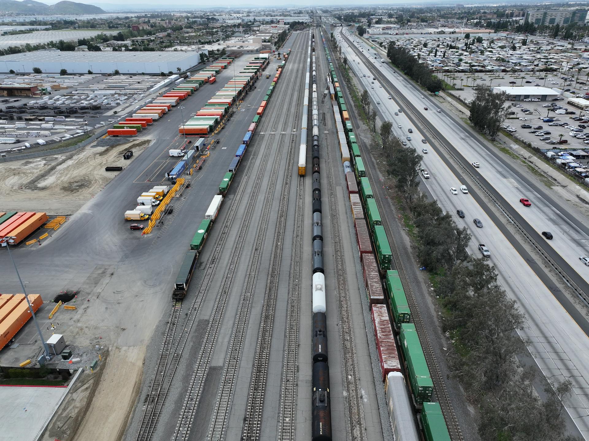 Aerial perspective of a busy train yard with freight trains and cargo containers in California.
