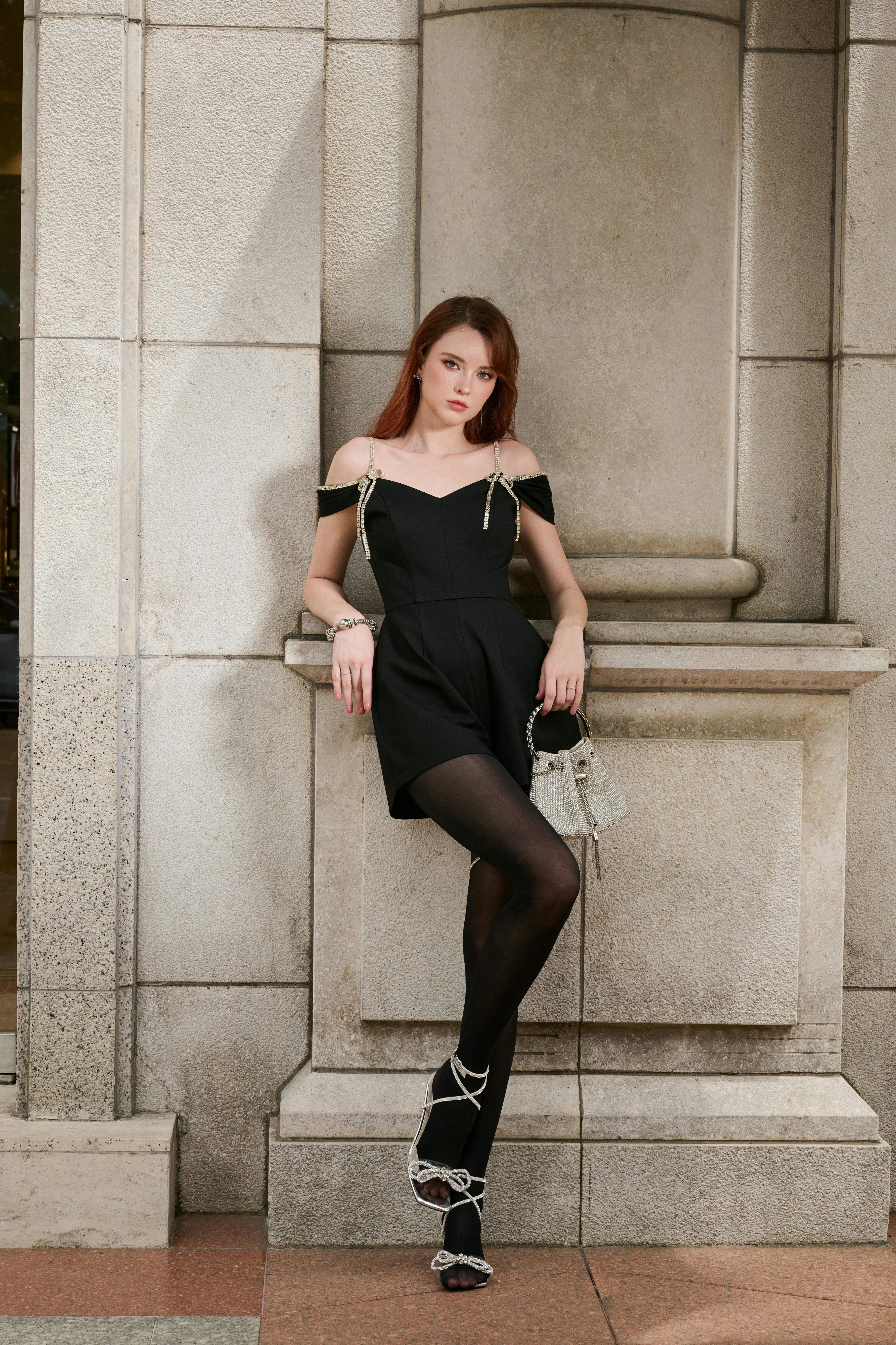 Stylish woman in a black dress posing against elegant stone architecture. Urban fashion and elegance.