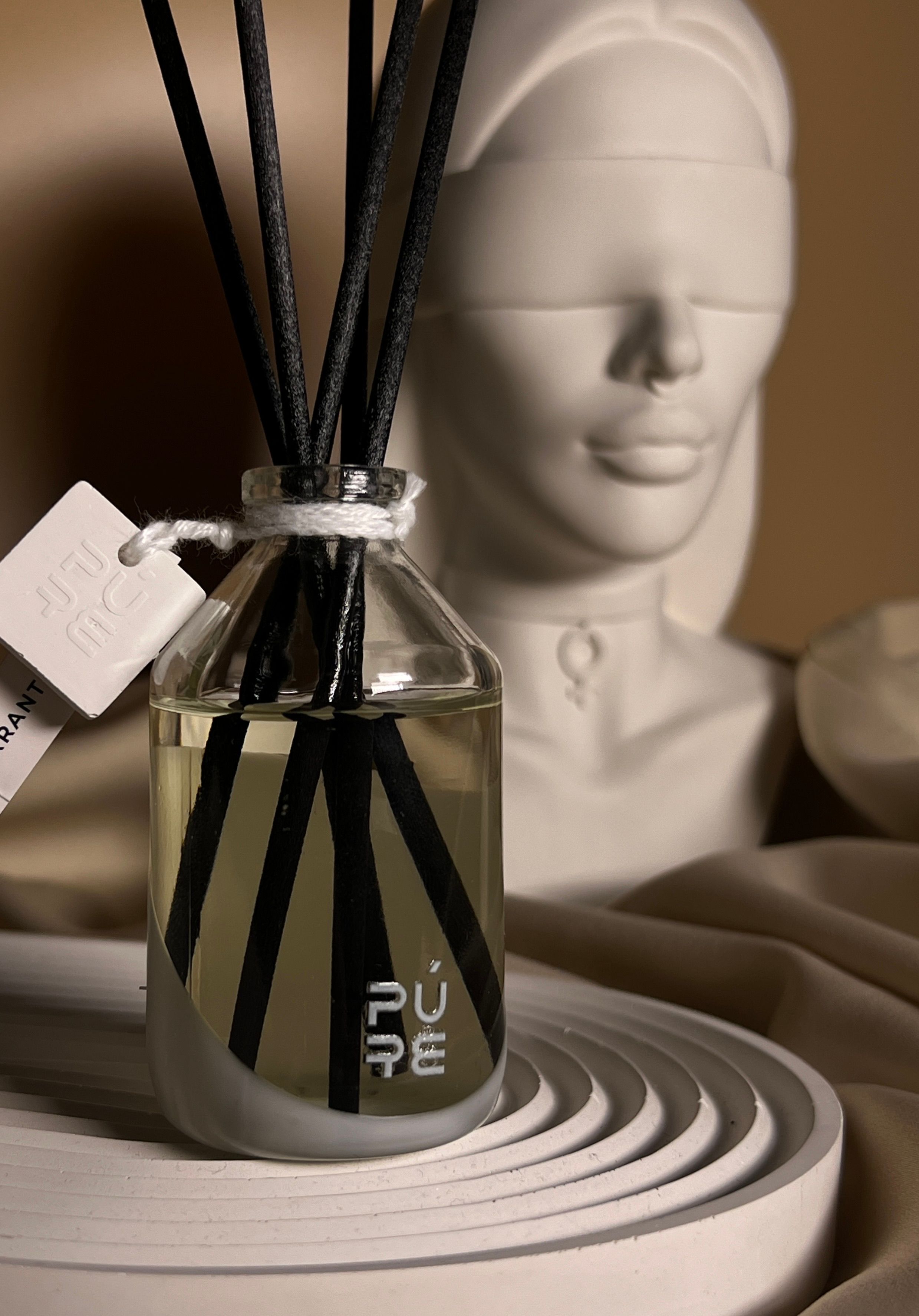 Difusor de aromas elegante com busto esculpido ao fundo, criando um ambiente sereno e minimalista.