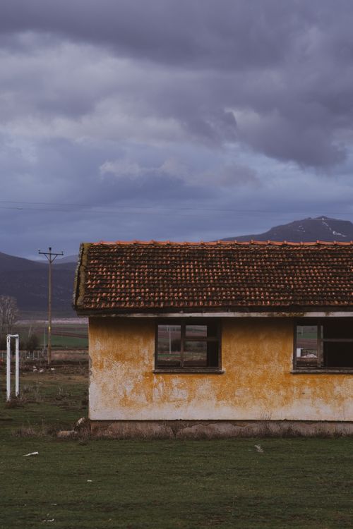 Free A solitary abandoned house with weathered walls against a moody sky and mountain backdrop. Stock Photo