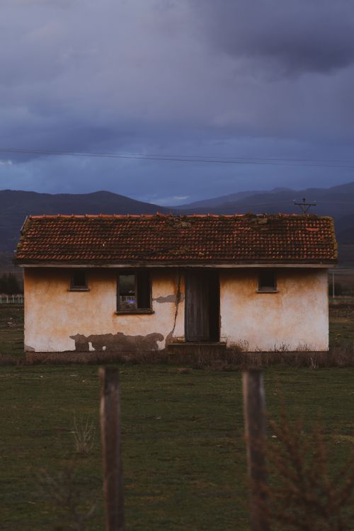 Free An old, rustic house stands abandoned in a vast rural landscape under a cloudy sky. Stock Photo