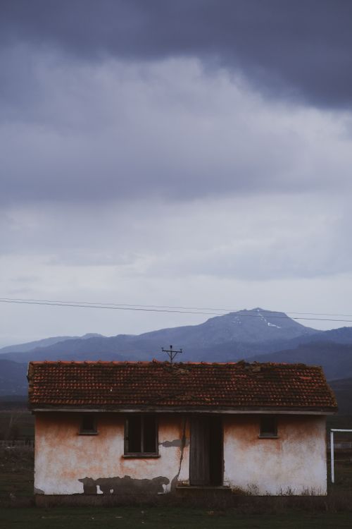 Free A small rustic cabin set against a dramatic mountain range under cloudy skies. Stock Photo