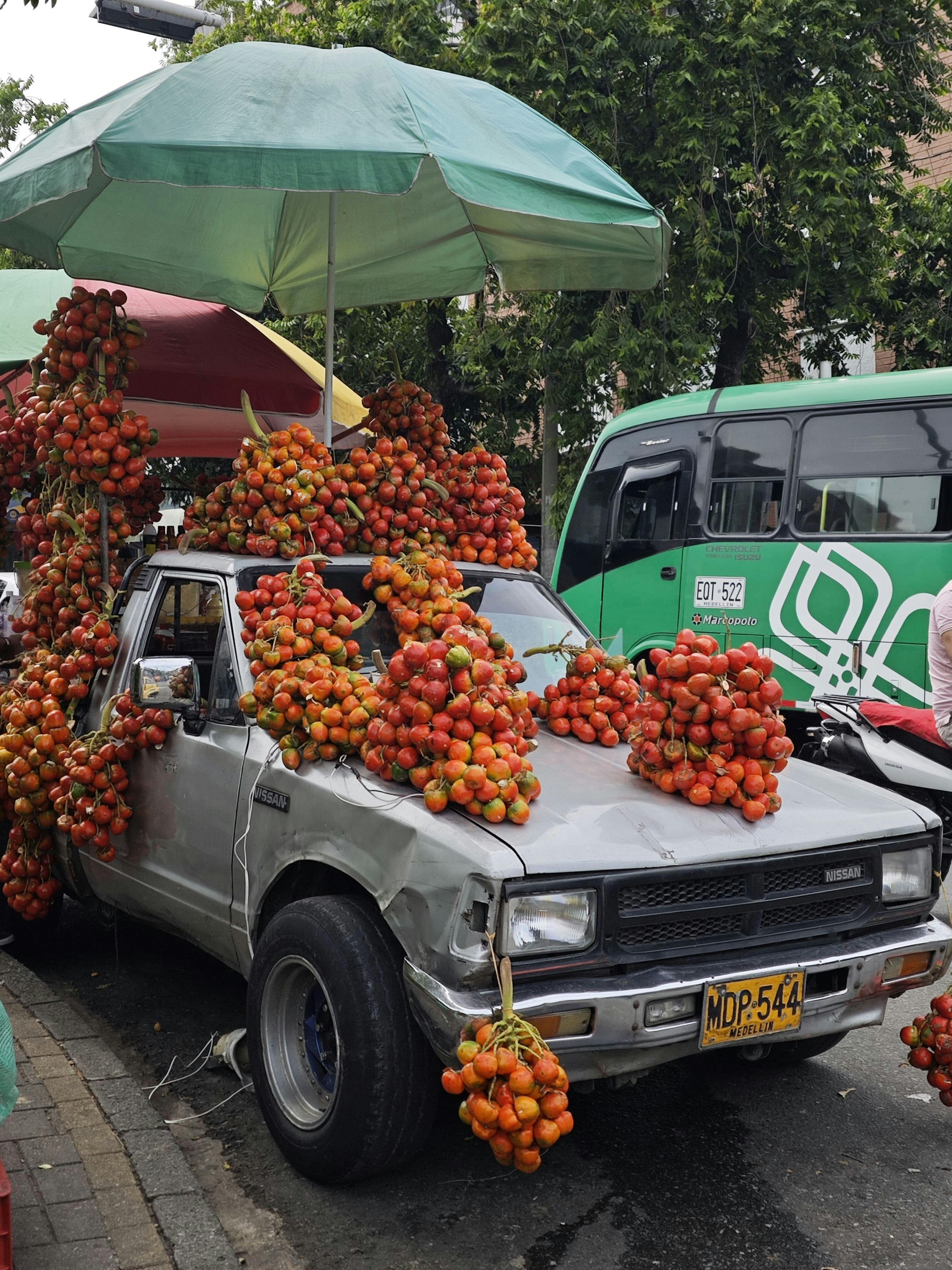 A vintage truck covered with ripe tomatoes, parked on a city street, showcasing a vibrant urban market scene.