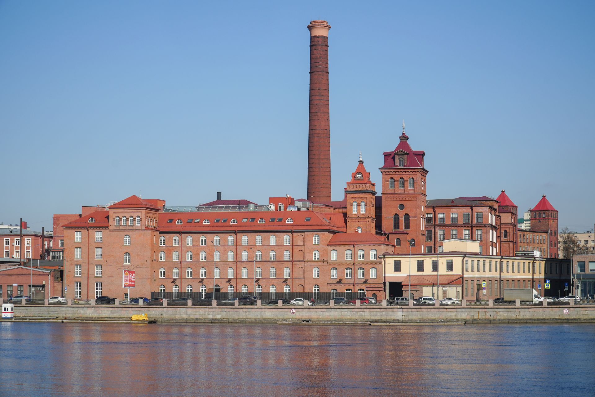 Historic red brick brewery building with tall chimney in Saint Petersburg, reflected on a sunny day.