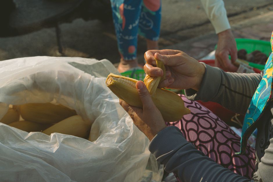 A close-up of a street vendor in Bình Thuận, Vietnam preparing corn for sale. Captured during the day.