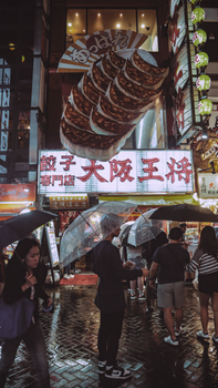 Bustling street scene in Dotonbori, Osaka at night with neon signs and umbrellas.