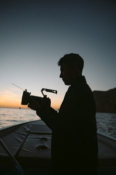 A man silhouetted filming on a boat at sea during a stunning sunset scene.