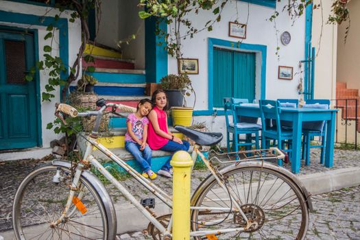 Two children relax by colorful steps next to a rustic bike, embraced by vibrant visuals and calm ambiance.