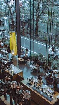Urban cafe scene in Tokyo with people dining against a large glass window view of the street.