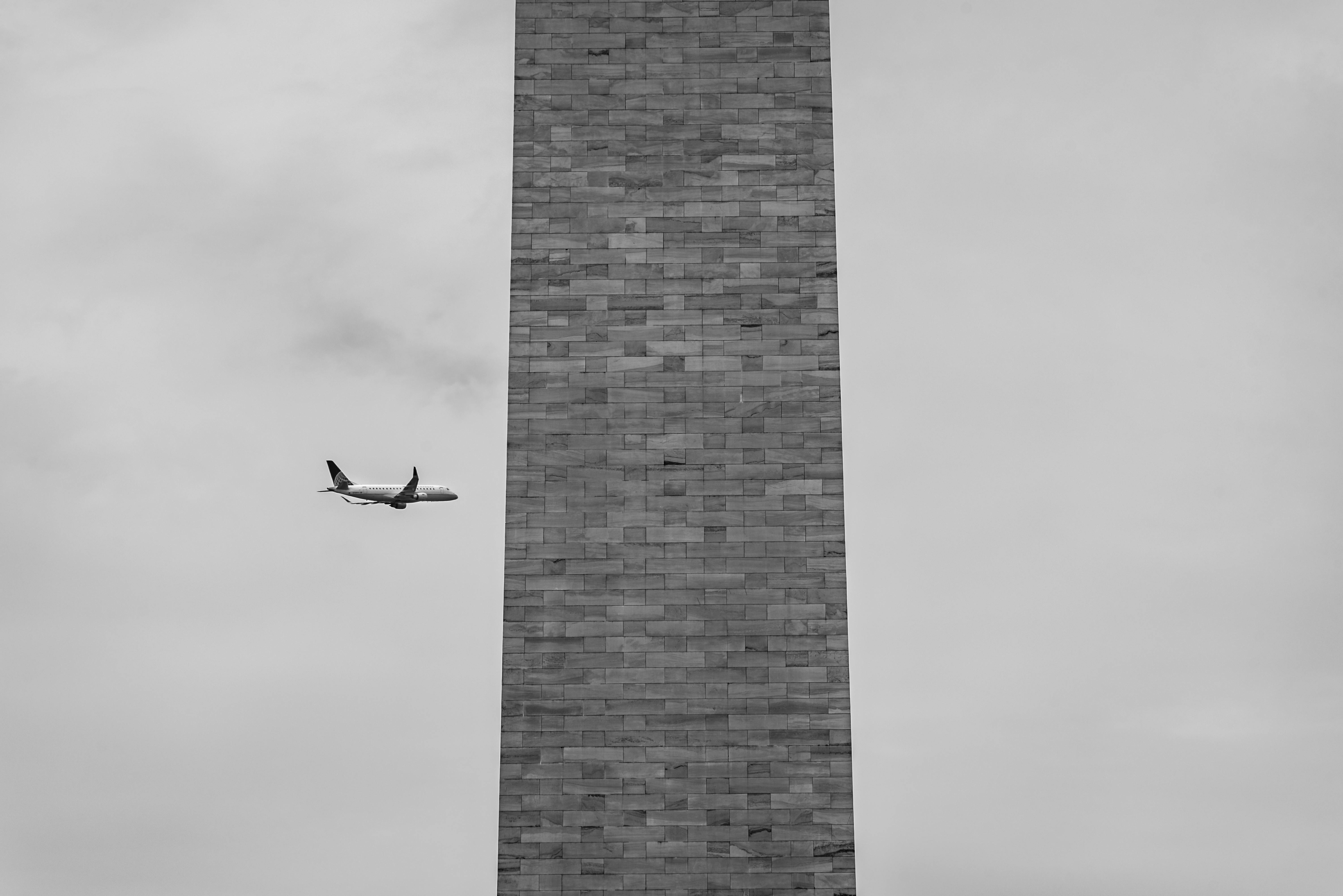 Kostenlos Ein eindrucksvolles Schwarzweißfoto eines Flugzeugs in der Nähe des berühmten Washington Monuments, das die Perspektive zeigt. Stock-Foto