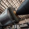 A low-angle view of a massive, metallic rocket booster and its engine nozzle on display inside an expansive aerospace museum.