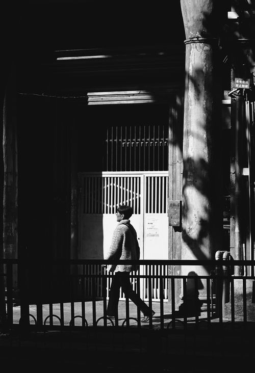 Free A man walks in shadow along a city street, creating a dramatic urban scene. Stock Photo