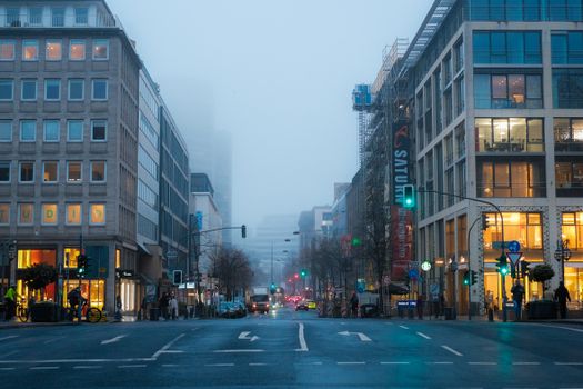 A foggy city street with modern buildings and traffic, captured during the day.
