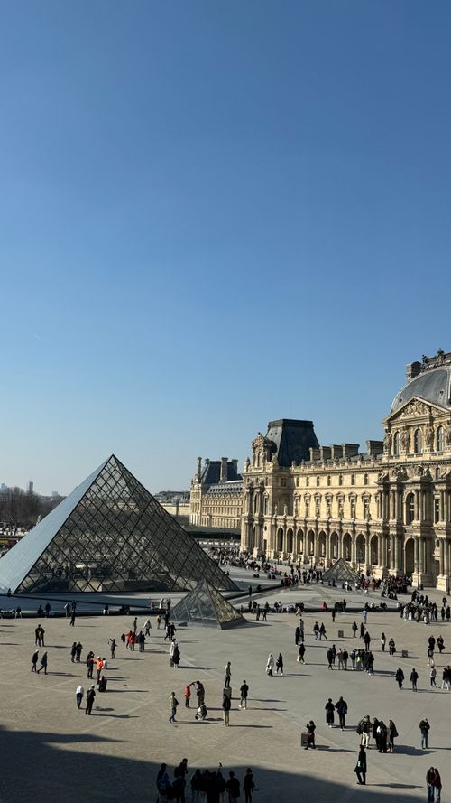Free Breathtaking view of the Louvre Pyramid and museum with visitors under a clear blue sky. Stock Photo