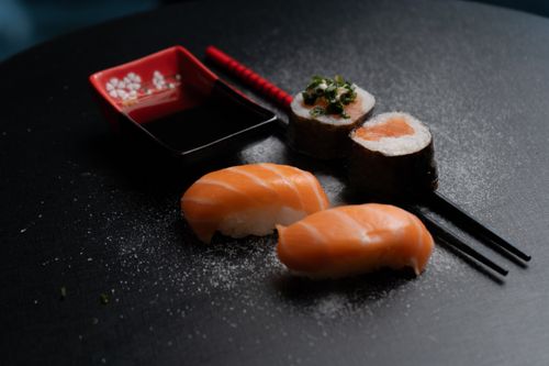 Free Aesthetic sushi set with salmon nigiri, sushi rolls, soy sauce, and chopsticks on a black background. Stock Photo