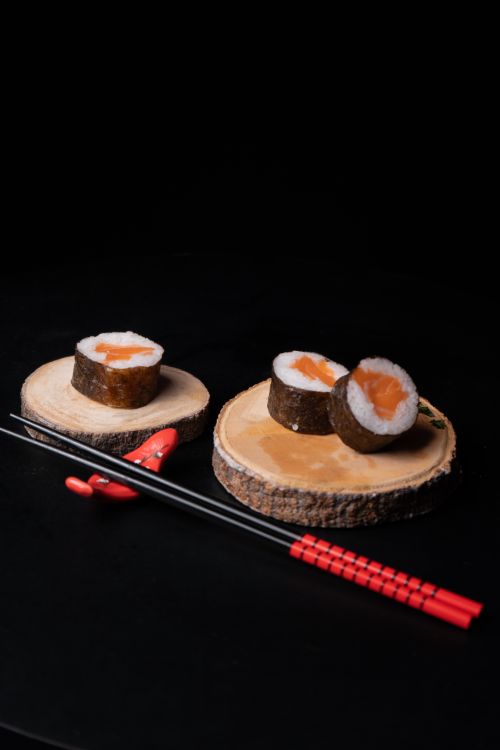 Free Artistic sushi rolls on wooden plates with red chopsticks on a dark background. Stock Photo