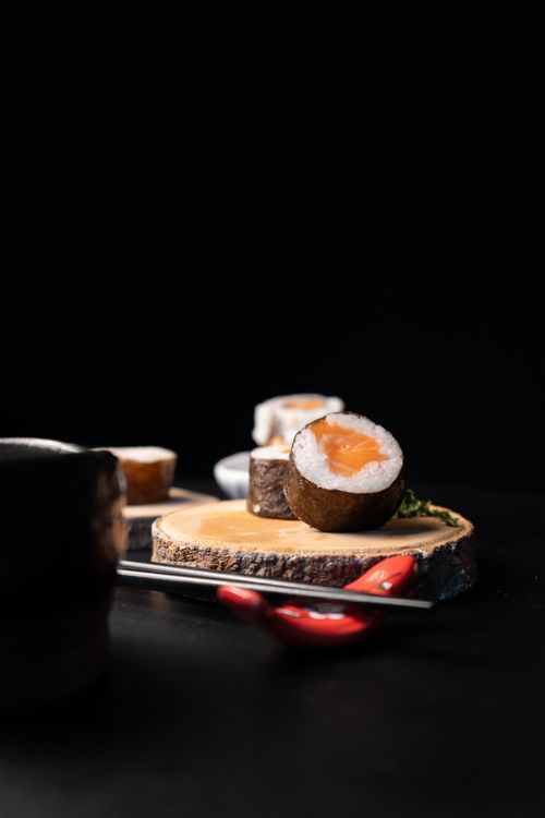Free Close-up of sushi rolls on a wooden slab with a dark background, garnished with chili peppers. Stock Photo