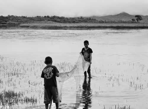 Free Two boys fishing in serene marshland with mountains in the background. Stock Photo