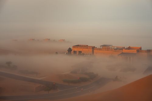 Free Aerial view of desert buildings enveloped in morning fog, casting a serene and mysterious ambiance. Stock Photo