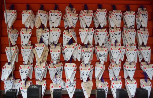 Free Several Japanese fox face ema plaques, with unique designs, displayed outside on an orange background. Stock Photo