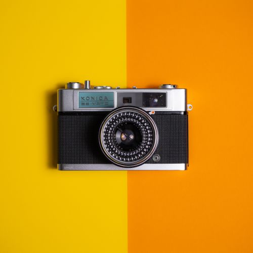 Free Retro Konica camera displayed on a vibrant yellow and orange surface. Stock Photo